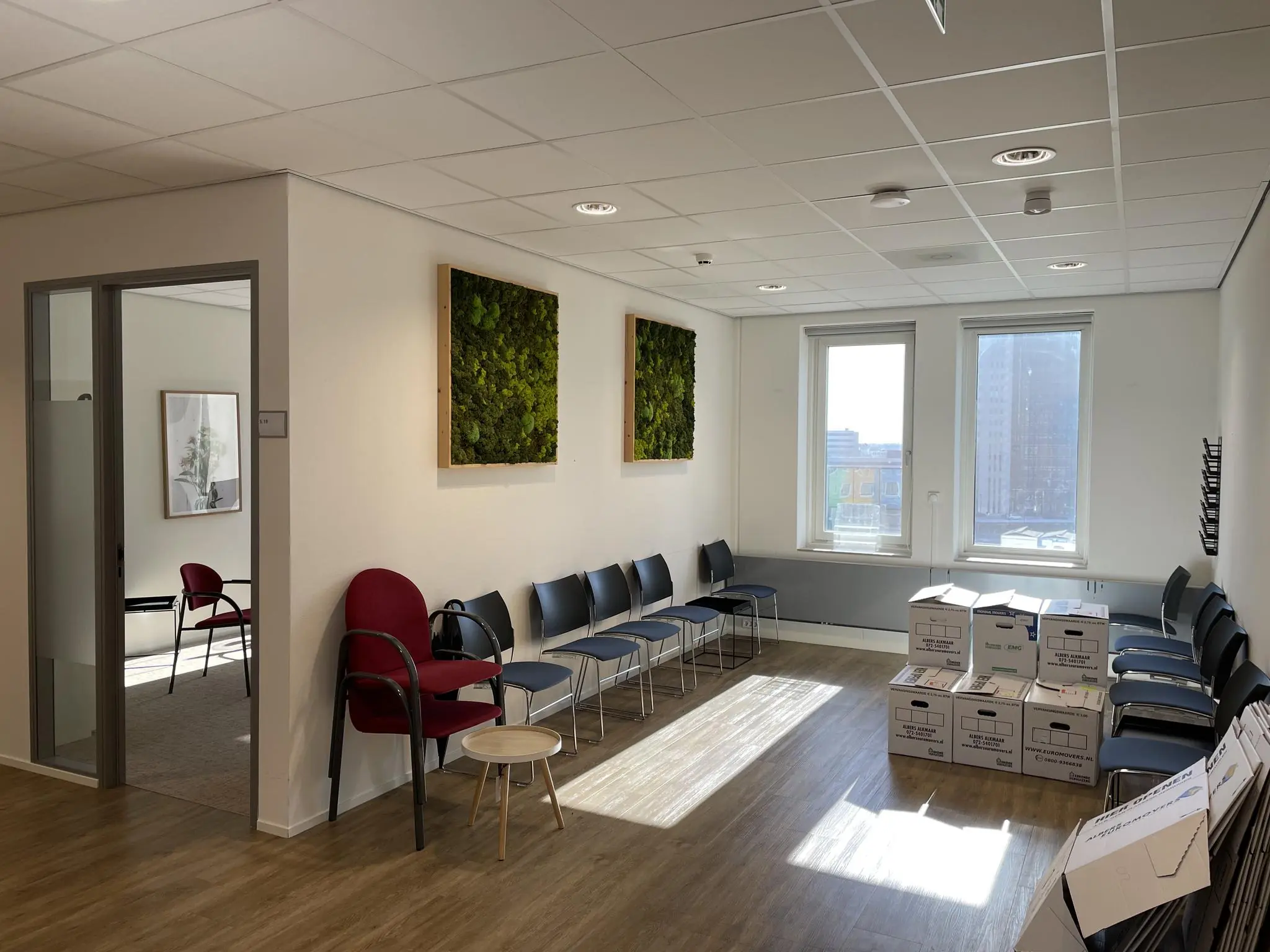 Wachtruimte op de Johan Cruijff Boulevard met stoelen, verhuisdozen en groene wanddecoratie.